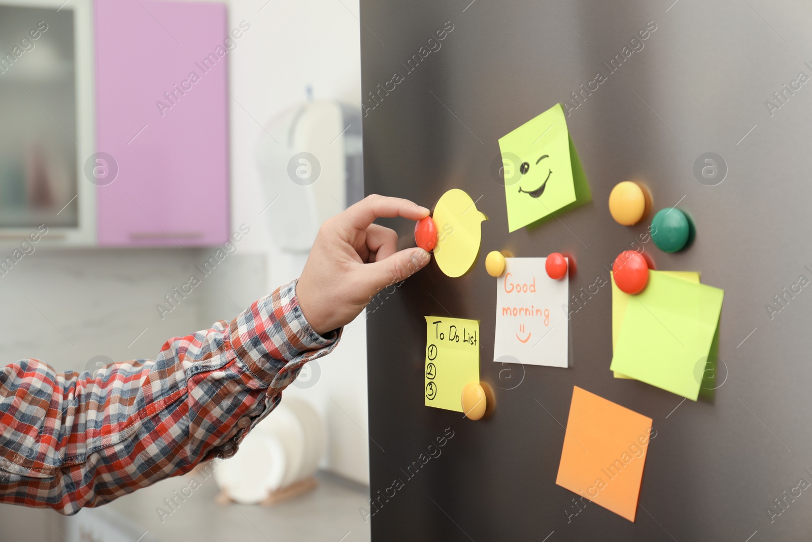 Photo of Man putting paper sheet on refrigerator door at home, closeup