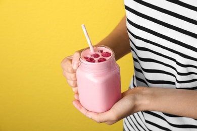 Photo of Woman holding mason jar with delicious raspberry smoothie on yellow background, closeup