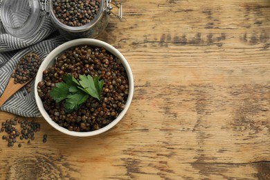 Bowl of delicious lentils, jar and spoon with raw seeds on wooden table, top view. Space for text