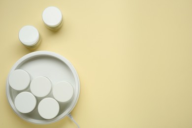 Modern yogurt maker with jars on beige background, flat lay. Space for text