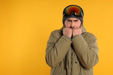 Photo of Winter sports. Man in ski suit and goggles on orange background, space for text