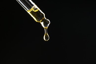 Dripping tincture from pipette on black background, closeup. Space for text