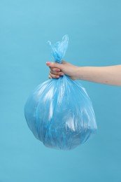 Photo of Woman holding plastic bag full of garbage on light blue background, closeup