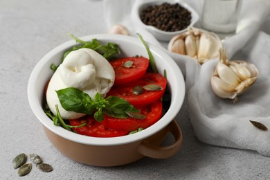 Photo of Delicious burrata cheese with tomatoes, pumpkin seeds and garlic on grey table, closeup