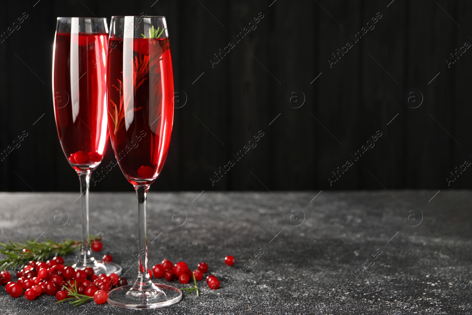 Photo of Tasty cranberry cocktail with rosemary in glasses on gray textured table against dark background, space for text