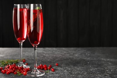 Tasty cranberry cocktail with rosemary in glasses on gray textured table against dark background, space for text