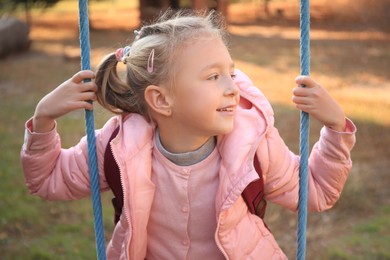 Photo of Cute little girl with backpack on swing outdoors