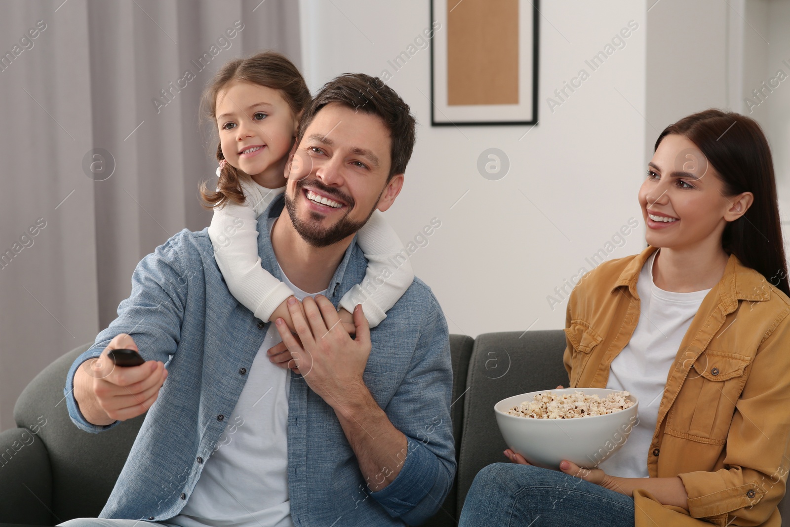 Photo of Happy family watching movie at home. Father changing TV channels with remote control