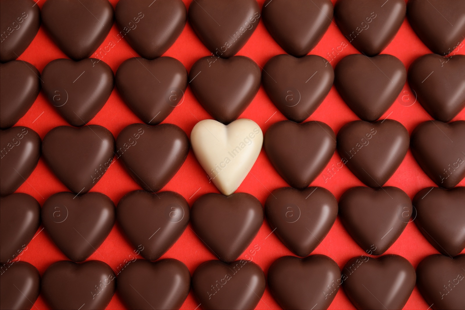 Photo of Tasty heart shaped chocolate candies on red background, flat lay. Happy Valentine's day