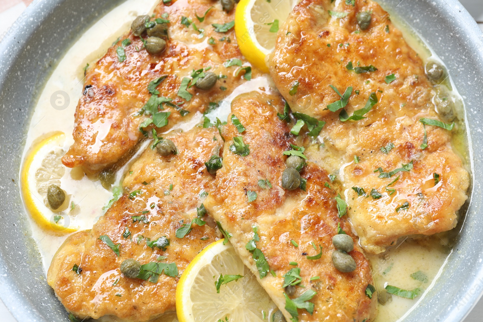 Photo of Delicious chicken piccata with lemons and herbs in pan, closeup