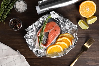 Photo of Flat lay composition of aluminum foil with raw fish, rosemary and orange on wooden table