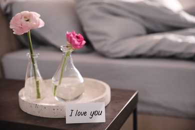 Photo of Note saying I Love You near tray with flowers on bedside table in room