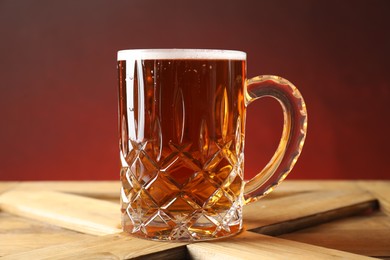 Mug with fresh beer on wooden crate against color background, closeup