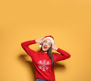 Photo of Young woman in Christmas sweater and hat on color background