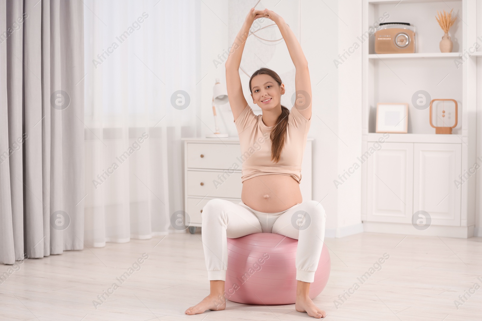 Photo of Pregnant woman doing exercises on fitness ball in room. Home yoga