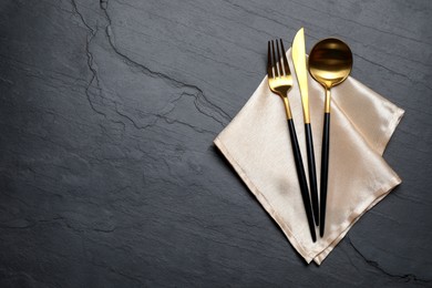 Photo of Set of golden cutlery with napkin on black table, top view. Space for text