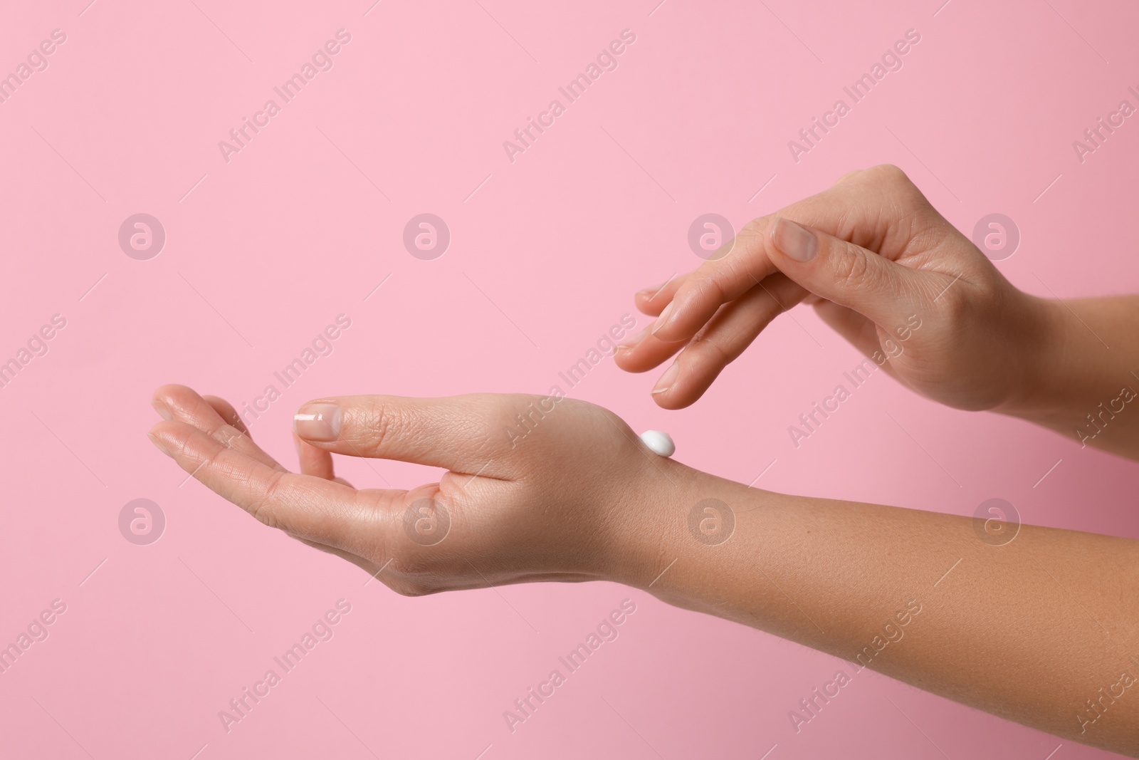 Photo of Woman applying cosmetic cream onto hand on pink background, closeup