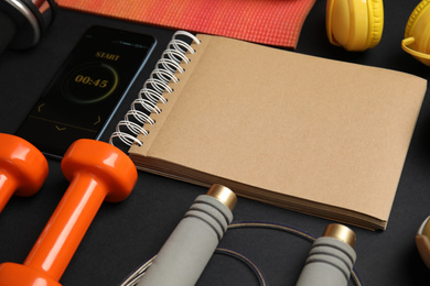 Photo of Composition with fitness equipment, notebook  and smartphone on dark background
