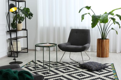 Stylish grey armchair and small coffee table in living room. Interior design