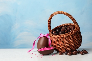 Photo of Wicker basket with sweet chocolate Easter eggs and dragee on table against color background, space for text