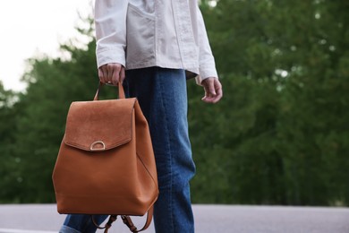 Young woman with stylish backpack walking along empty road, closeup. Space for text