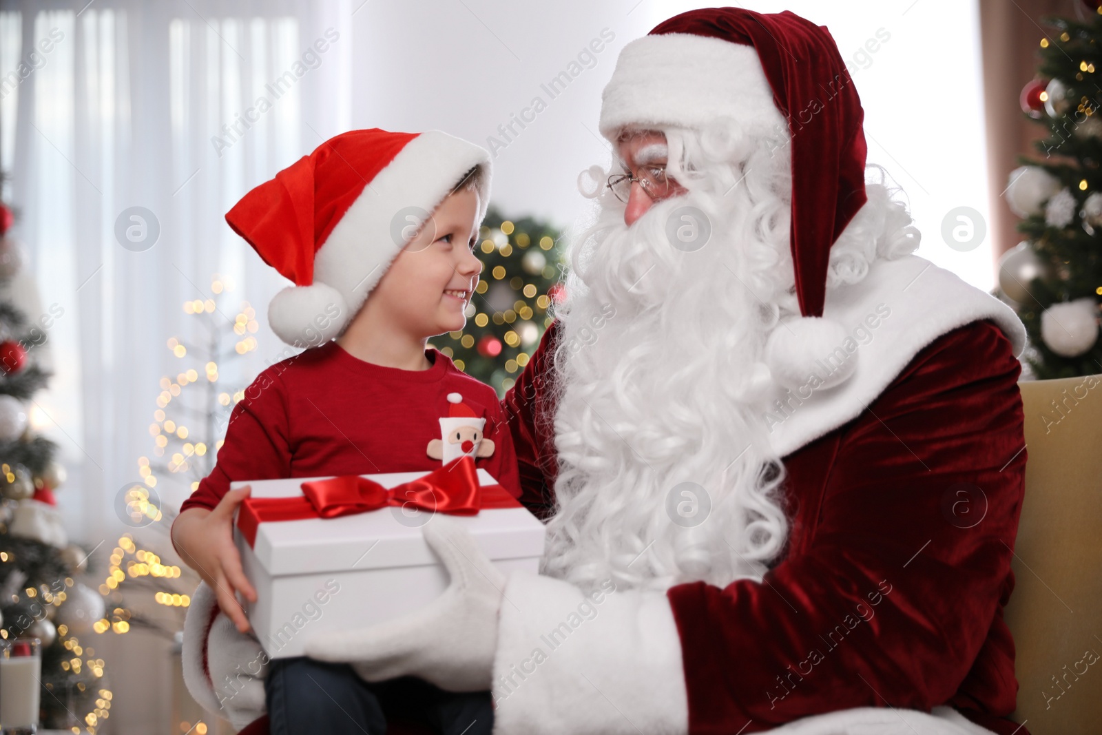 Photo of Santa Claus giving present to little boy in room decorated for Christmas