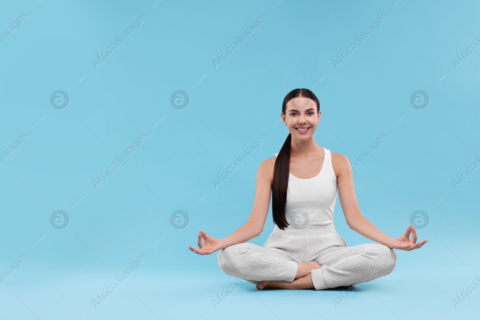 Photo of Beautiful young woman practicing yoga on light blue background, space for text. Lotus pose