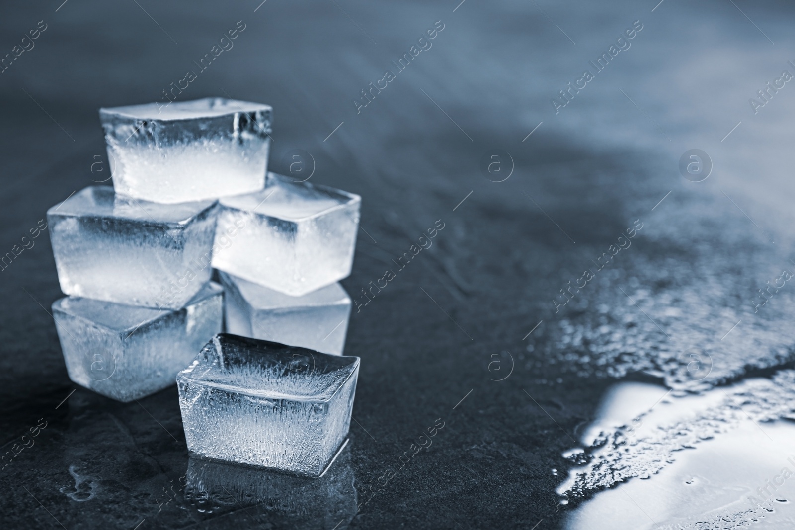 Photo of Ice cubes on wet grey surface, closeup. Space for text
