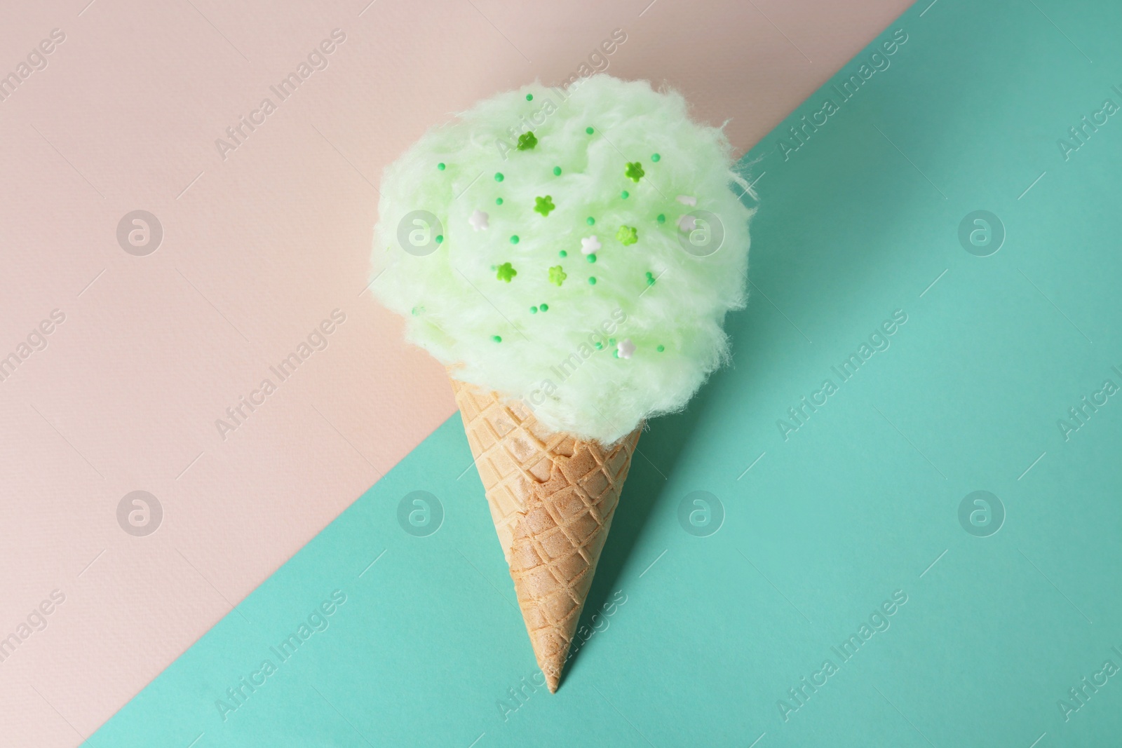 Photo of Sweet cotton candy in waffle cone on color background, top view