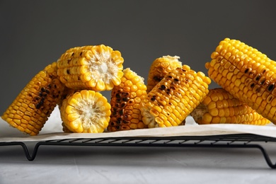 Photo of Cooling rack with grilled corn cobs on table against gray background