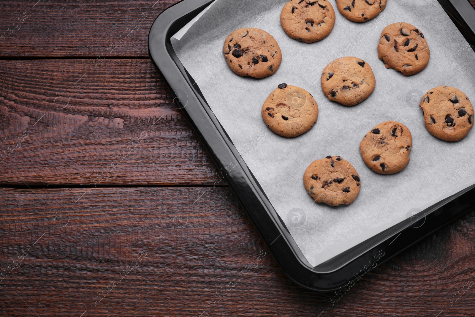 Photo of Baking pan with cookies and parchment paper on wooden table, top view. Space for text