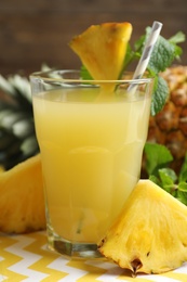 Photo of Delicious pineapple juice in glass and fresh fruit on table, closeup