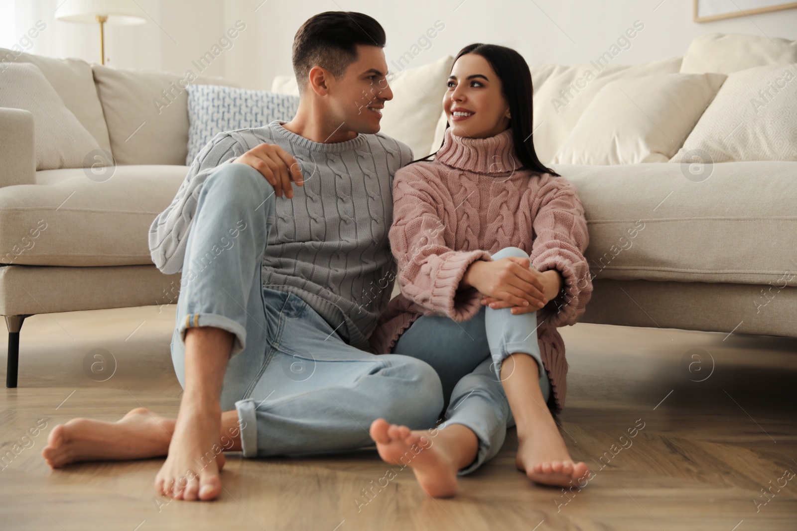 Photo of Happy couple sitting on warm floor in living room. Heating system