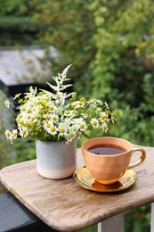 Photo of Cup of delicious chamomile tea and fresh flowers outdoors