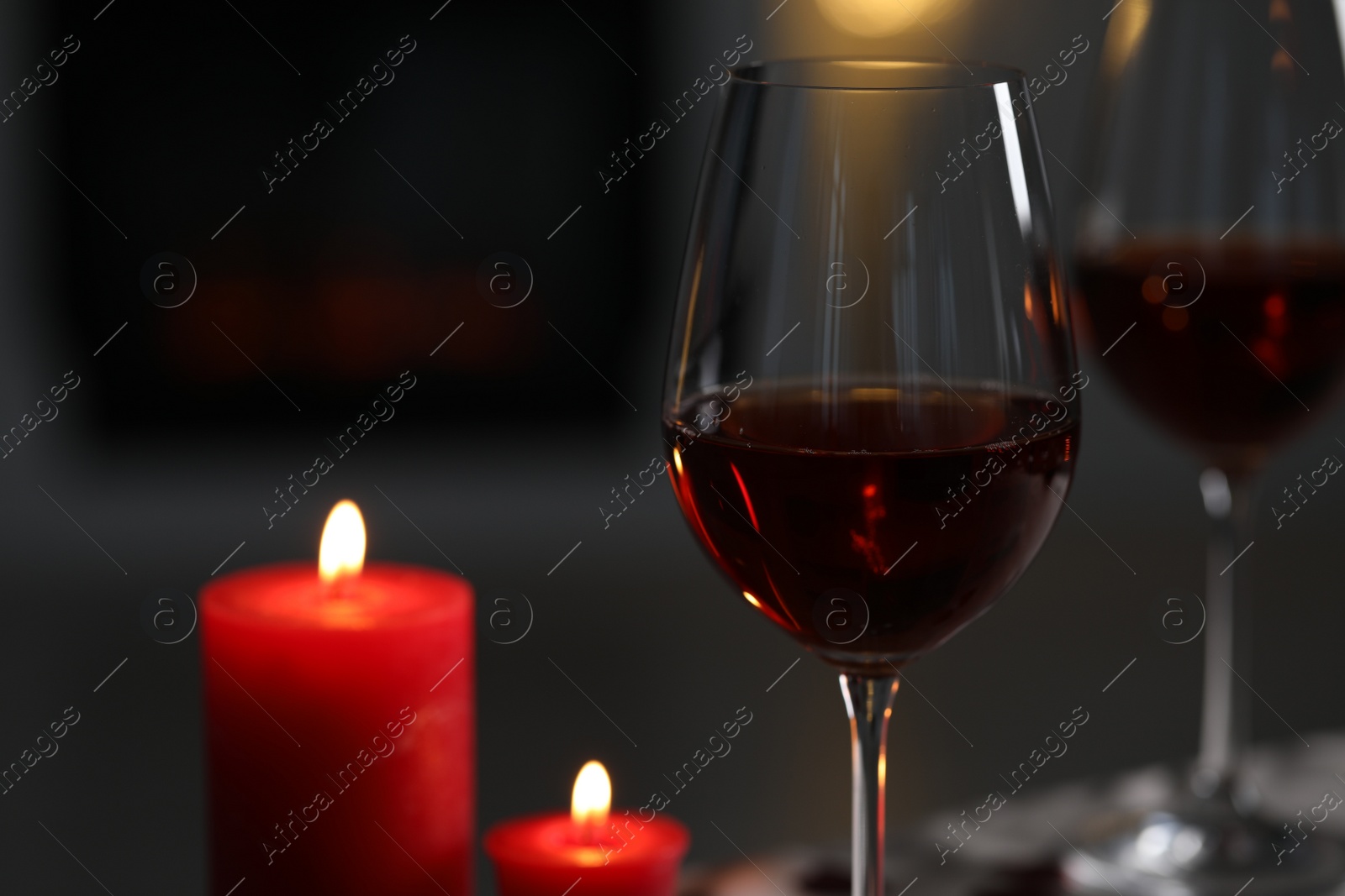 Photo of Glasses of red wine and burning candles against blurred background, space for text. Romantic atmosphere