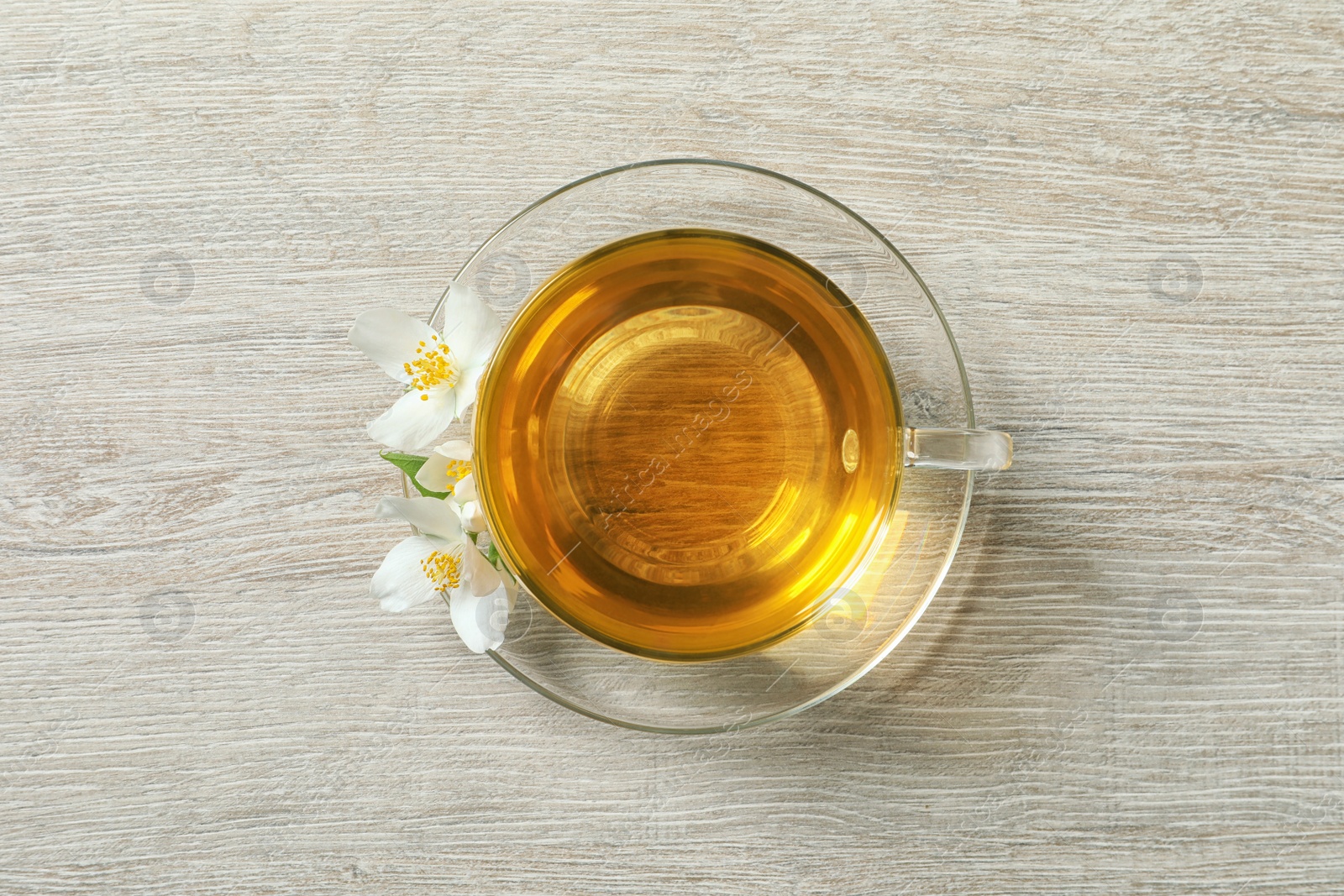 Photo of Glass cup of aromatic jasmine tea and fresh flowers on light wooden table, top view