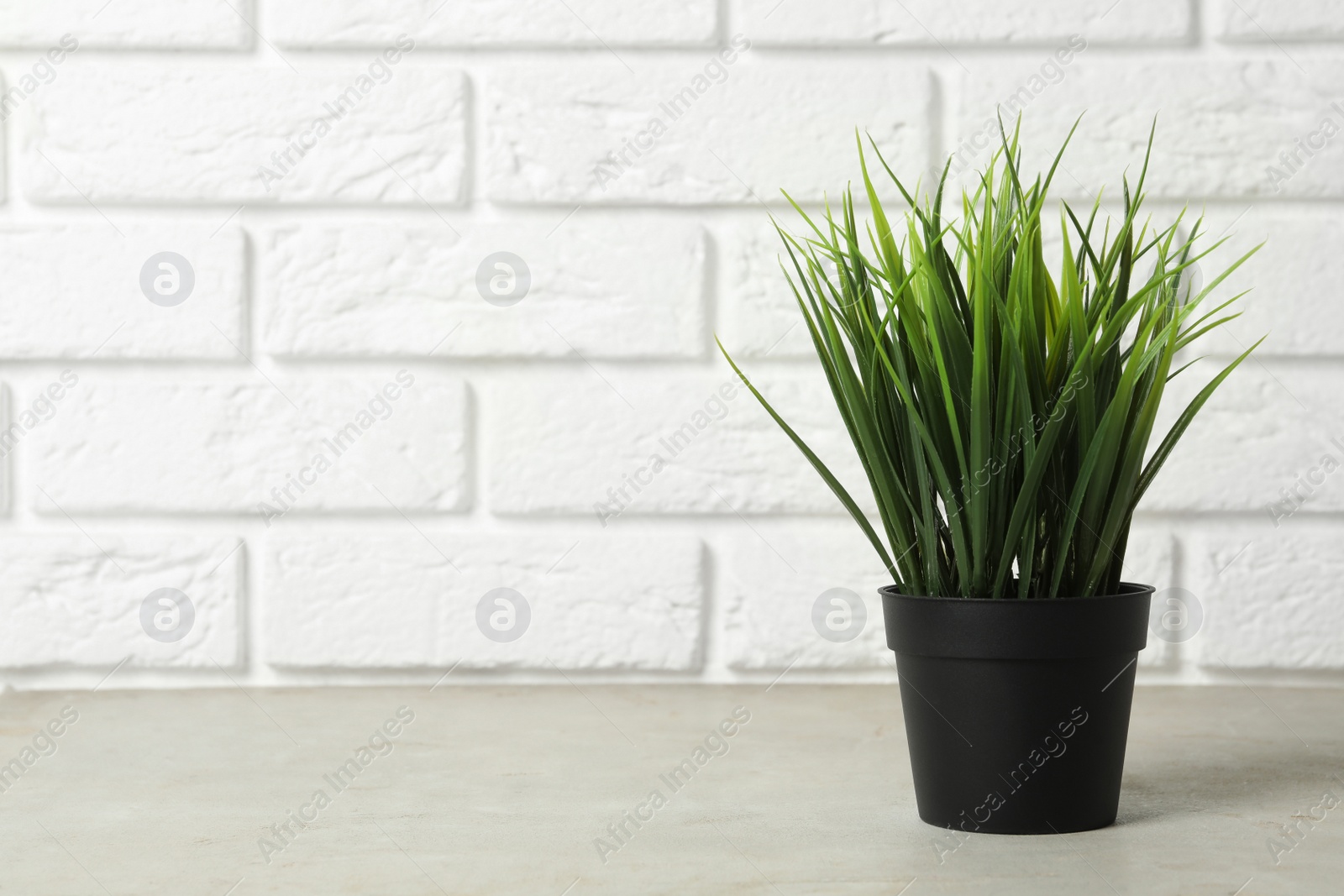 Photo of Beautiful artificial plant in flower pot on grey stone table near brick wall. Space for text
