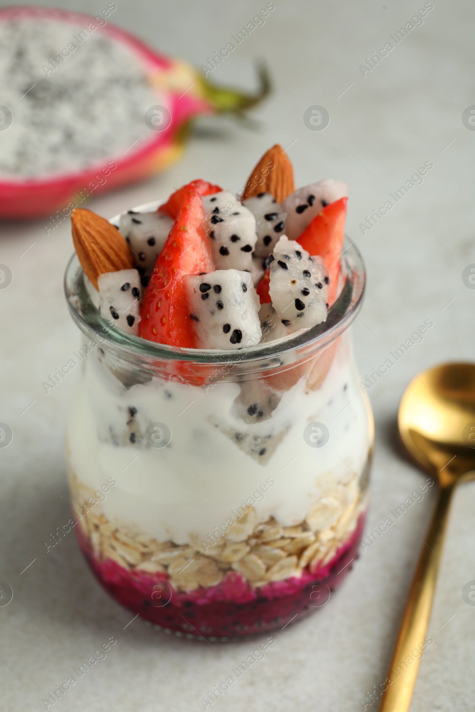 Photo of Glass jar of granola with pitahaya, yogurt and strawberries on white table