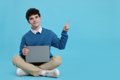 Photo of Portrait of student with laptop pointing on light blue background. Space for text