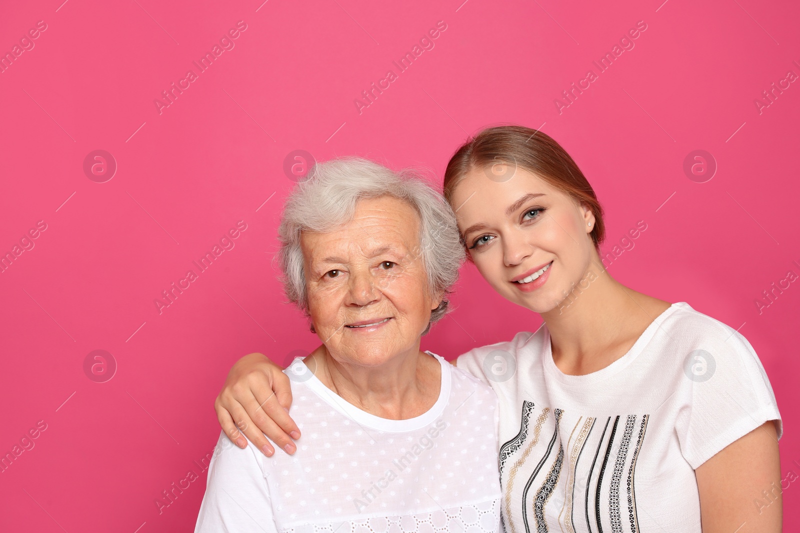 Photo of Young woman and her grandmother on pink background