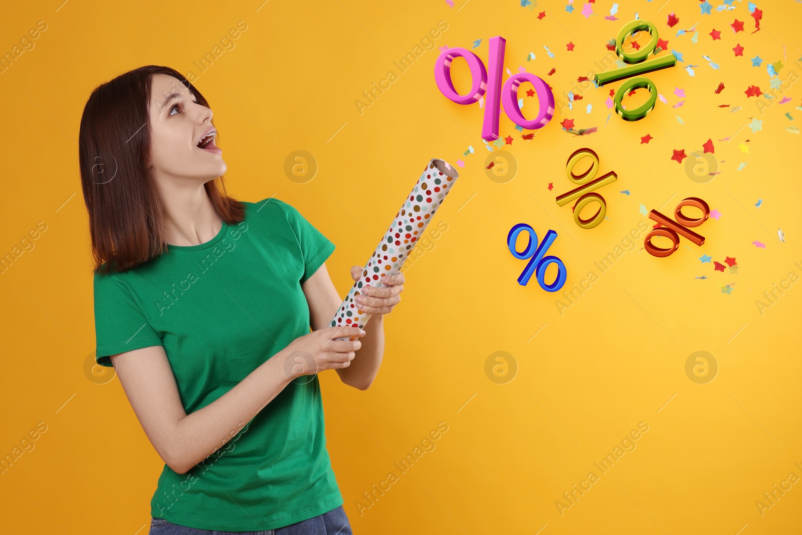 Image of Discount offer. Happy teenage girl blowing up party popper on golden background. Confetti and percent signs in air