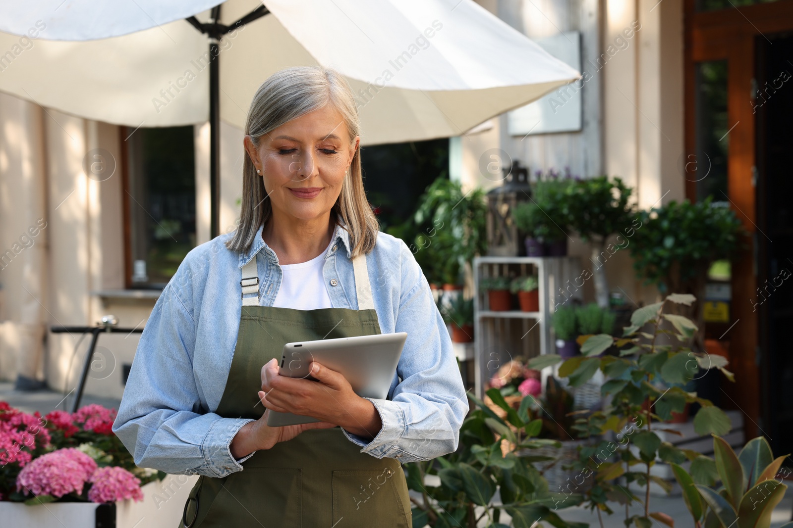 Photo of Smiling business owner using tablet near her flower shop outdoors, space for text