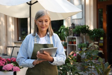 Photo of Smiling business owner using tablet near her flower shop outdoors, space for text