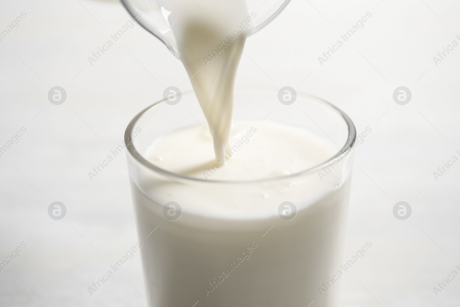 Photo of Pouring milk into glass on white table, closeup