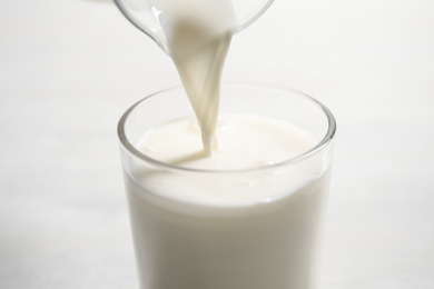 Photo of Pouring milk into glass on white table, closeup