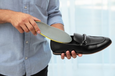 Photo of Man putting orthopedic insole into shoe indoors, closeup. Foot care