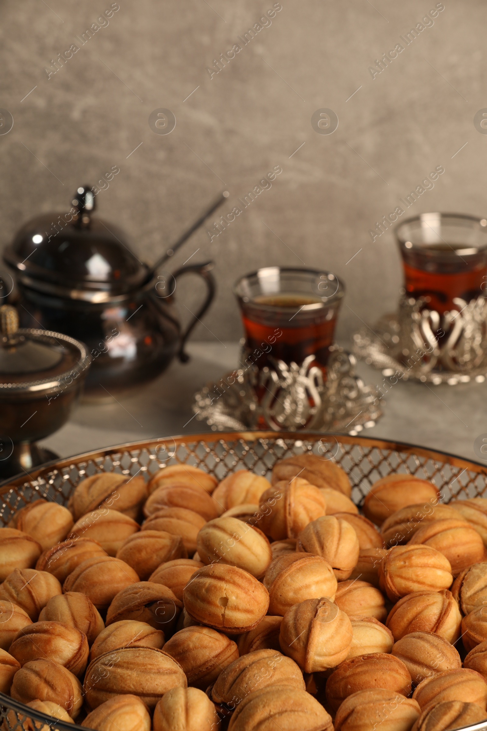 Photo of Delicious walnut shaped cookies and glasses of tea on grey table, closeup. Tasty pastry with filling carrying nostalgic home atmosphere