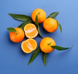 Fresh tangerines with green leaves on blue background, flat lay