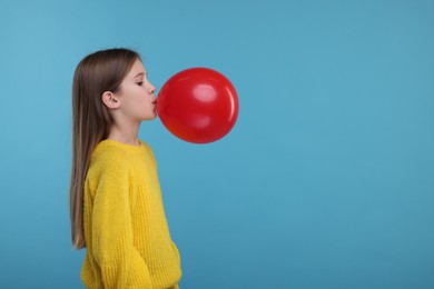 Photo of Cute girl inflating red balloon on light blue background, space for text