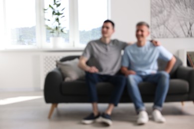 Photo of Blurred view of happy men sitting on sofa at home